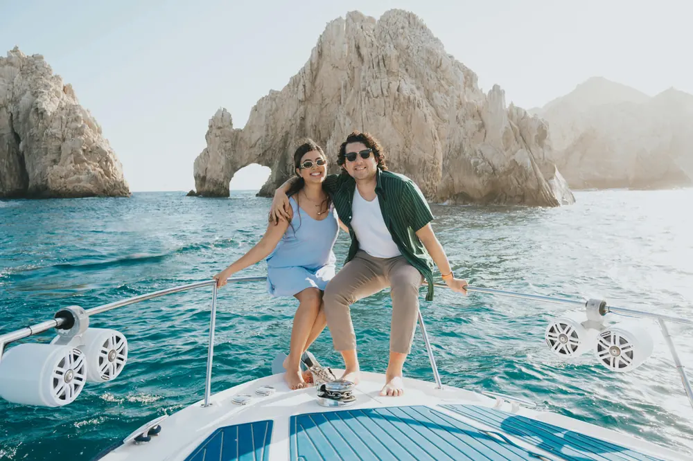 Couple sitting on the bow of a boat beside a rock arch